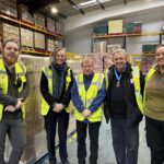 Image shows Eamonn O'Neal, High Sheriff of Greater Manchester with Lucy Danger, CEO of EMERGE & staff from FareShare Greater Manchester in the FareShare GM Warehouse
